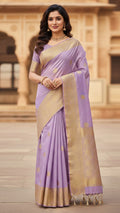 Woman wearing a lavender saree with gold border in front of a beige wall.
