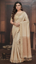 Woman wearing a beige saree with a brown border in an indoor setting